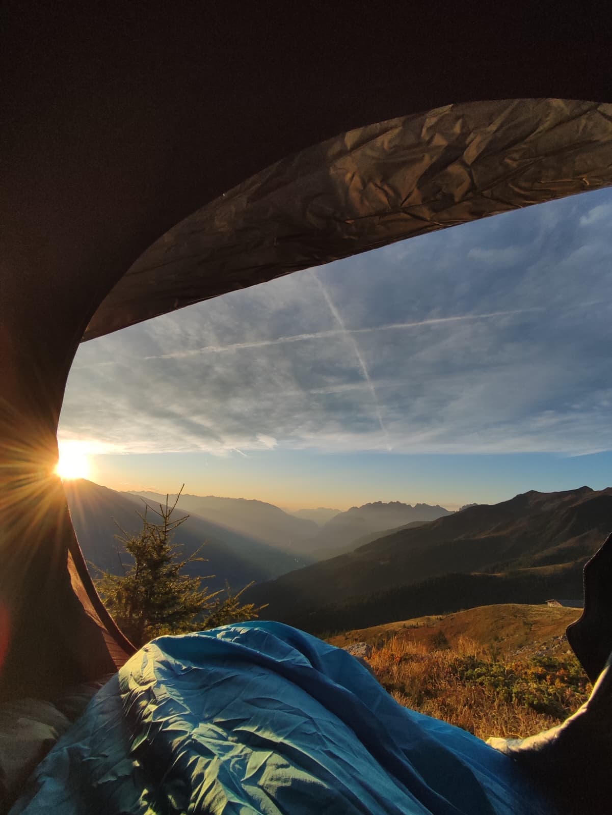 Blick aus dem Zelt bei Sonnenaufgang über den Bergen, im Vordergrund ein Schlafsack